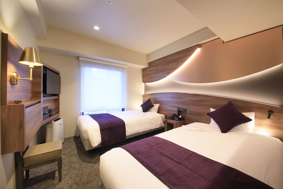 Une chambre d’hôtel avec deux lits, une télévision, un bureau et une fenêtre.