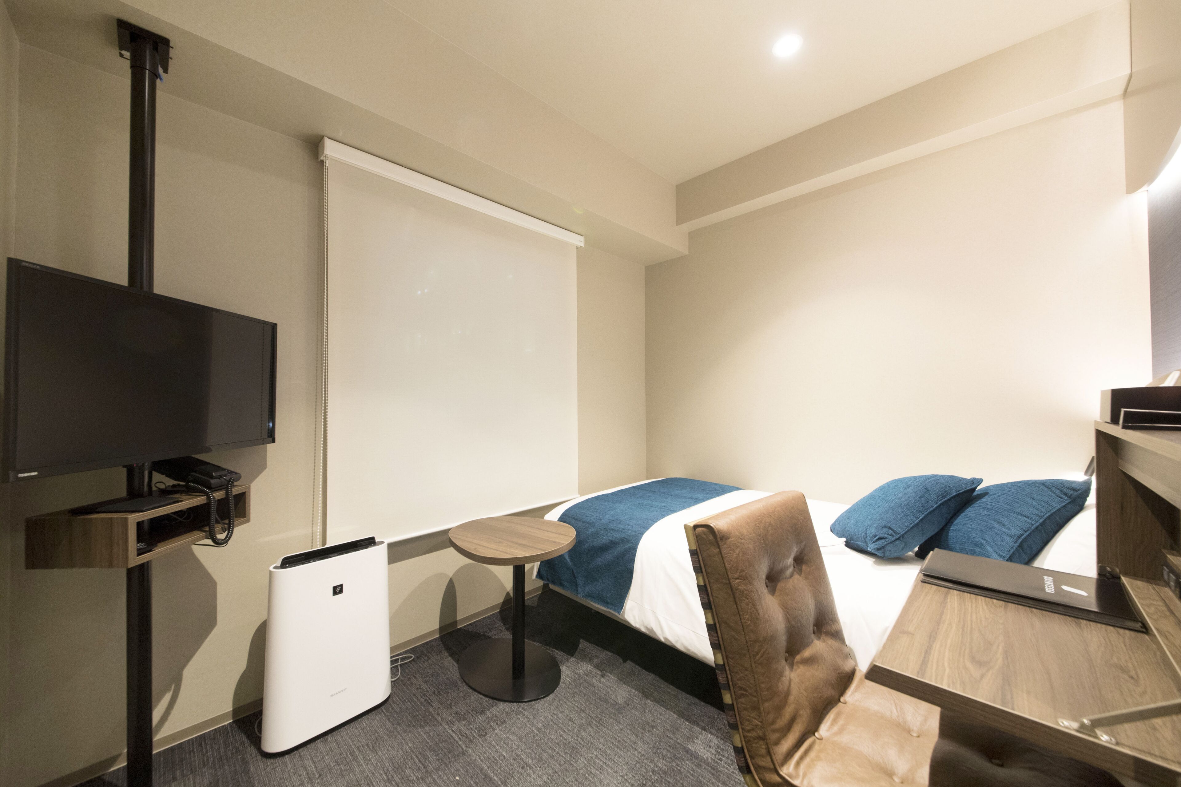 Una habitación de hotel con una cama, una mesita, una silla, un televisor y una pantalla para proyector.