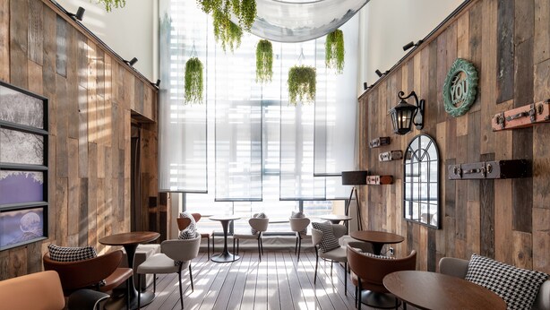 Ein modernes Interieur mit Holzwandverkleidung, hängenden Pflanzen und verschiedenen Sitzgelegenheiten, darunter Sofas und Tische.