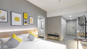 Ein modernes Hotelzimmer mit einem großen Bett, Nachttischen, einer Bank, einem Spiegel und einem durch eine offene Tür einsehbaren Badezimmer.