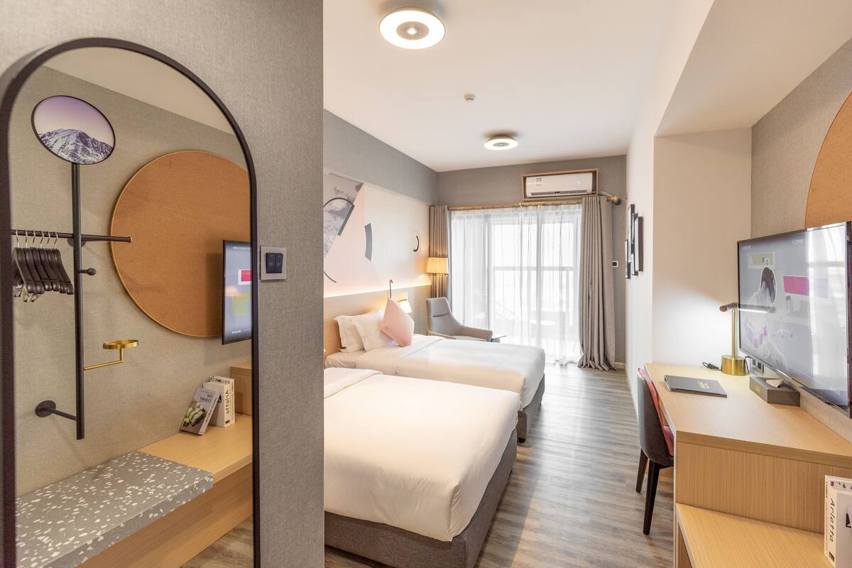 Een hotelkamer met twee bedden, een bureau, een televisie en een grote spiegel.