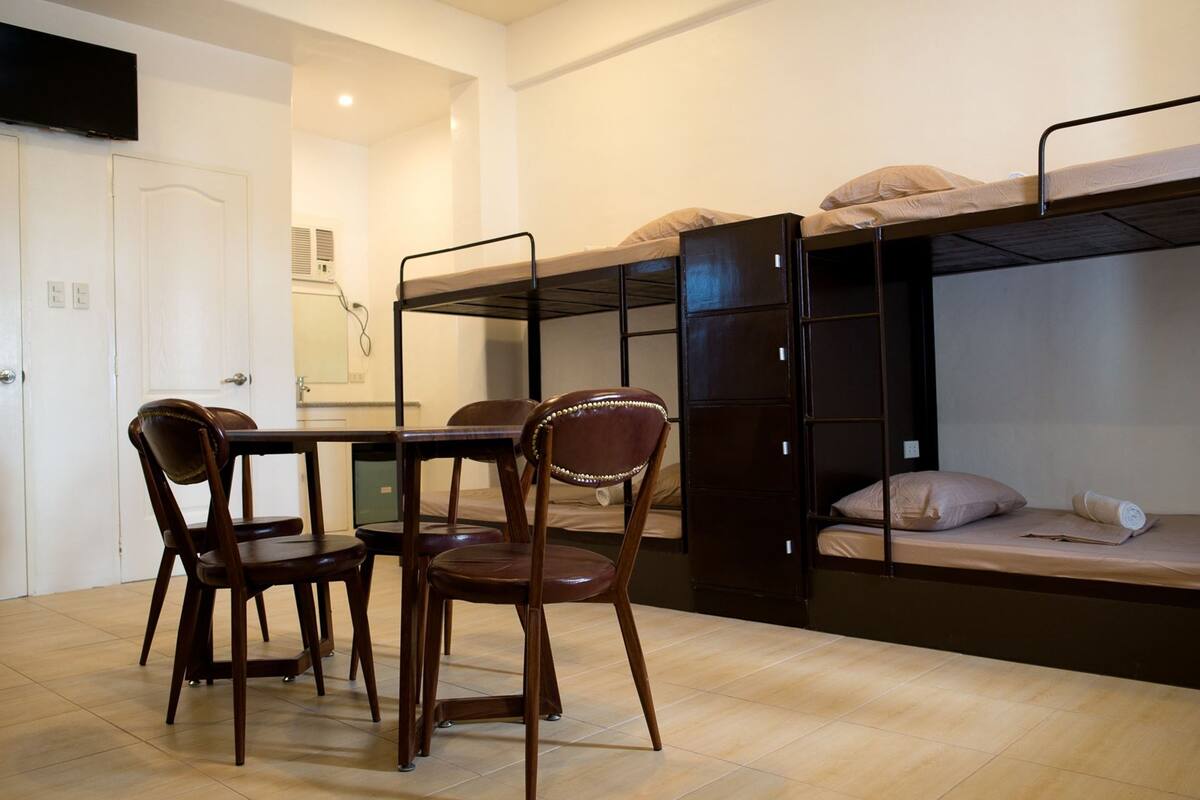 Une chambre de dortoir avec des lits superposés, une table à manger avec des chaises et un téléviseur fixé au mur.
