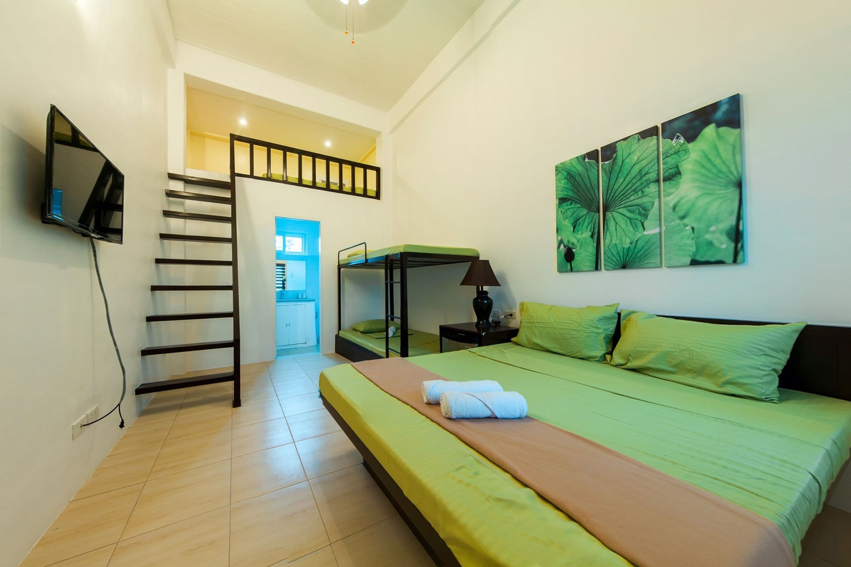 Un dormitorio con literas, un televisor de pantalla plana montado en la pared, un cuadro de hojas y una escalera que conduce a una habitación contigua.