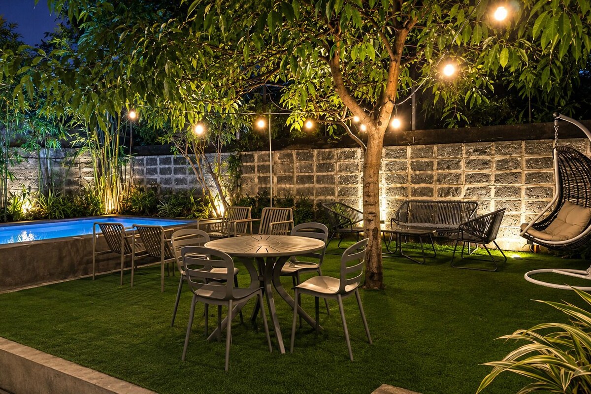 A backyard with a swimming pool, outdoor seating, and string lights.