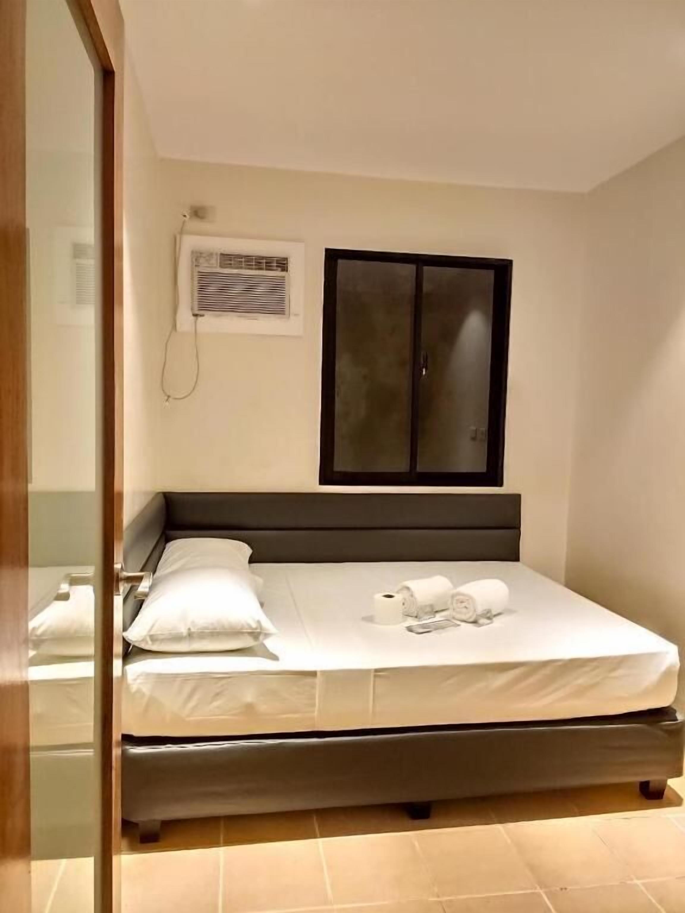 Un lit bien fait, avec des oreillers et une serviette roulée, une table de chevet avec une lampe et une fenêtre avec des stores.