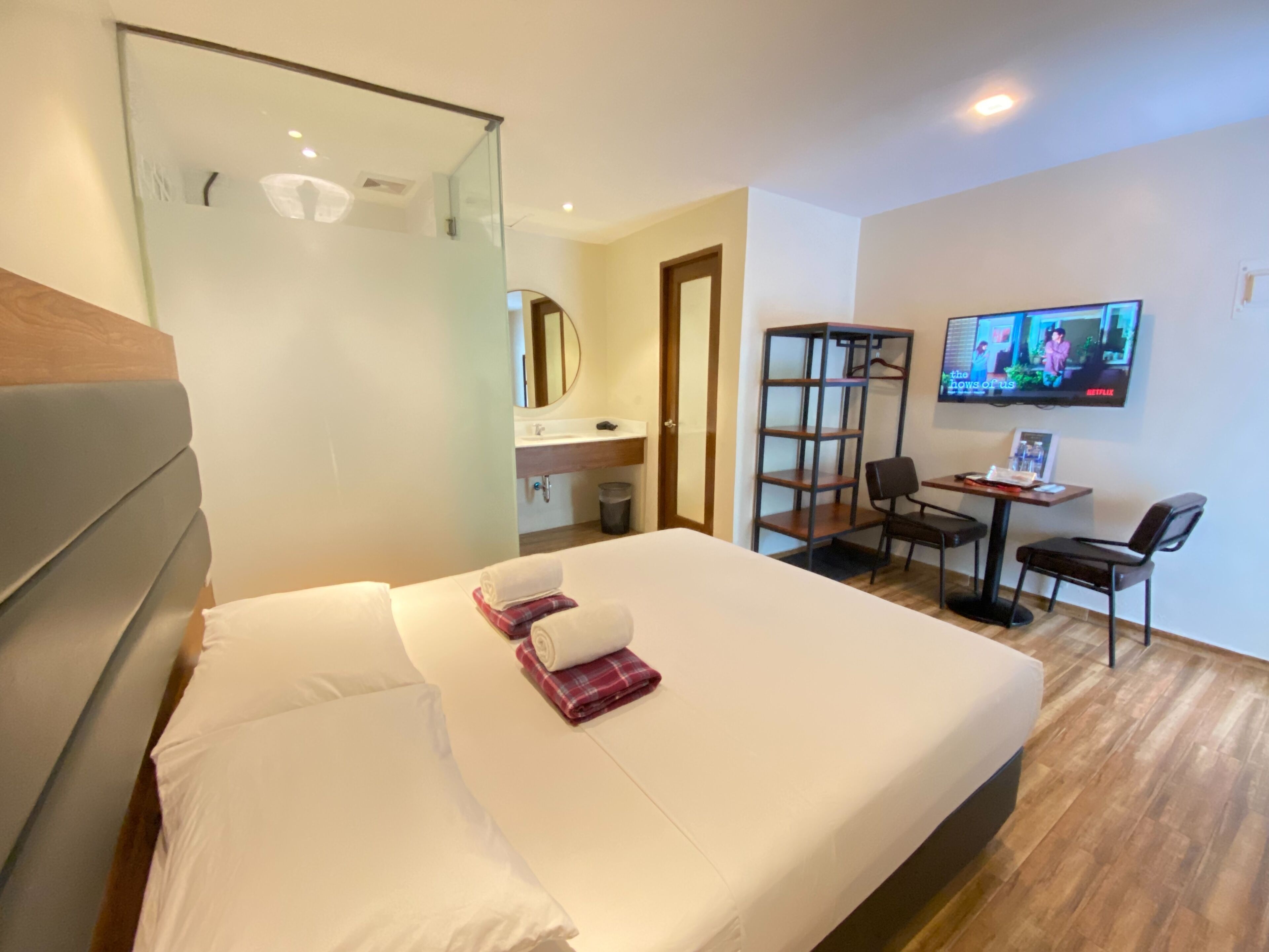 Ett hotellrum med en säng, ett skrivbord, en stol, en tv och en spegel.
