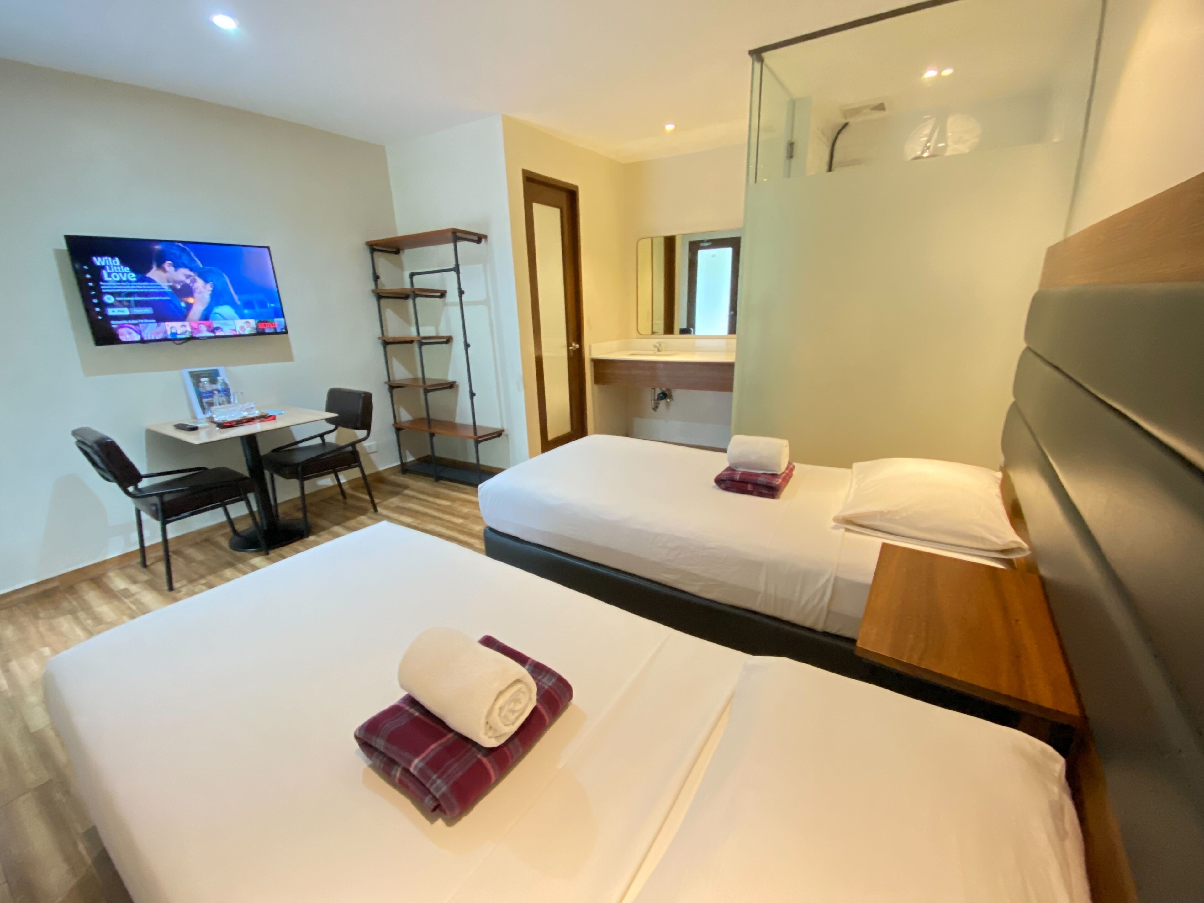 Une chambre d’hôtel avec deux lits, un bureau avec une chaise, une télévision et un miroir.