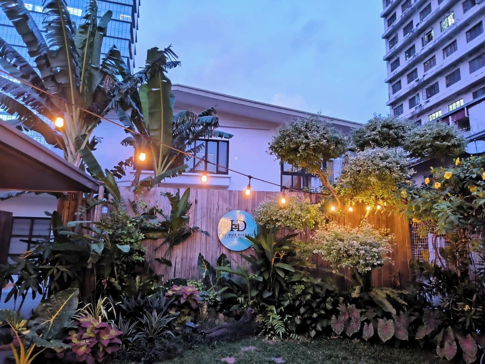 A garden area with a wooden fence, various plants, and a sign that reads "HUB DISTERIC."