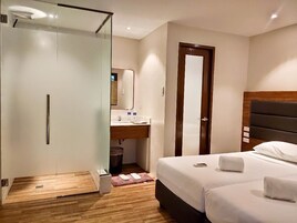 Camera d'albergo con cabina doccia in vetro, pavimento in legno, letto con lenzuola bianche, poggiatesta in legno e porta in legno.
