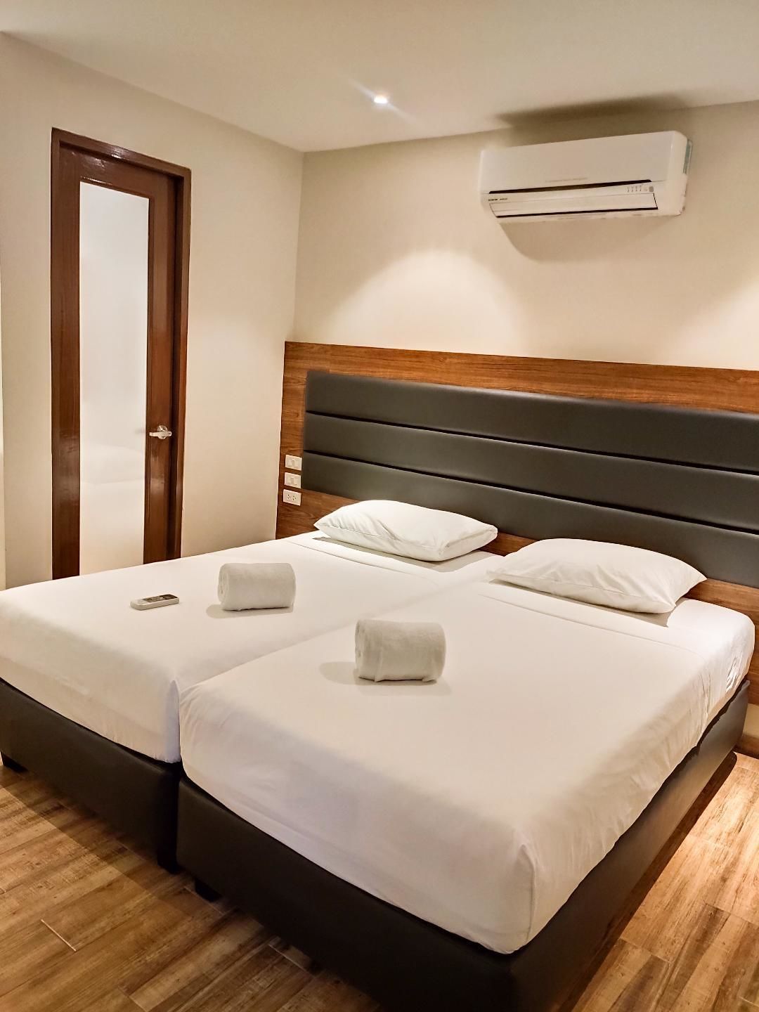 A hotel room with two beds, wooden flooring, a wooden headboard, white linens, and an air conditioning unit.