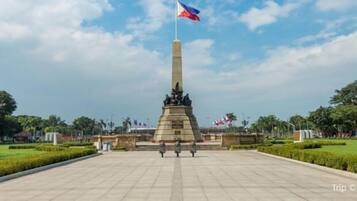 A monument with a flag, surrounded by a landscaped park with trees and a clear sky.
