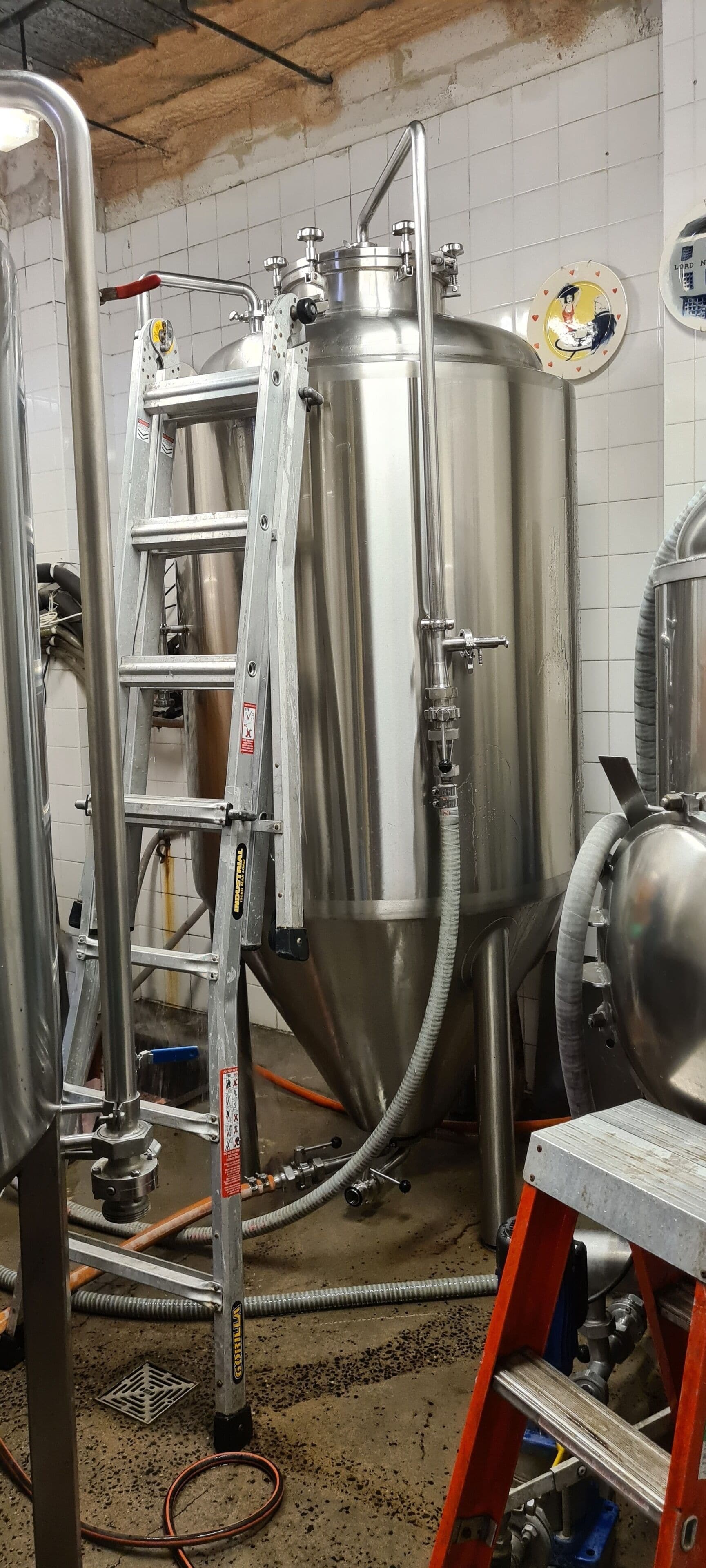 Équipement de brassage en acier inoxydable, une échelle et une table en métal dans un espace cuisine.
