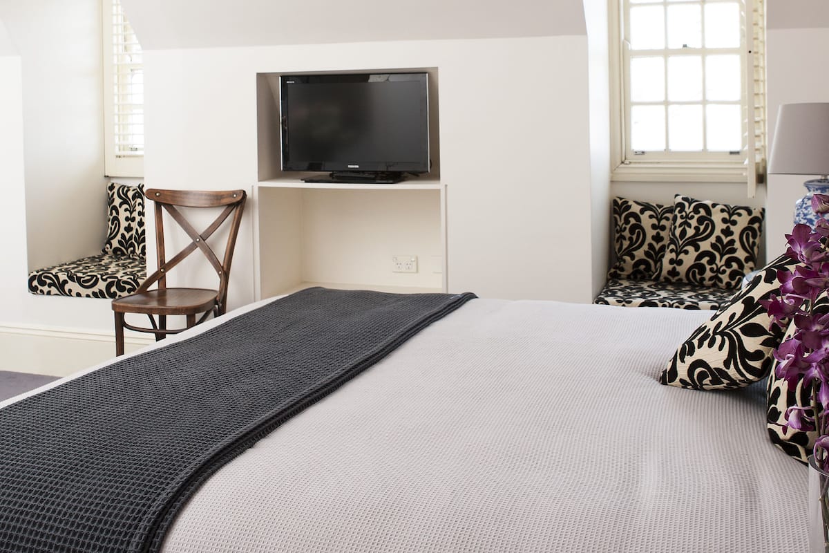 Un dormitorio con cama, televisión sobre un mueble, una silla y una ventana.