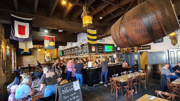 A bustling restaurant with a bar area, wooden beams, and a hanging barrel. - The Lord Nelson Brewery Hotel (Millers Point)