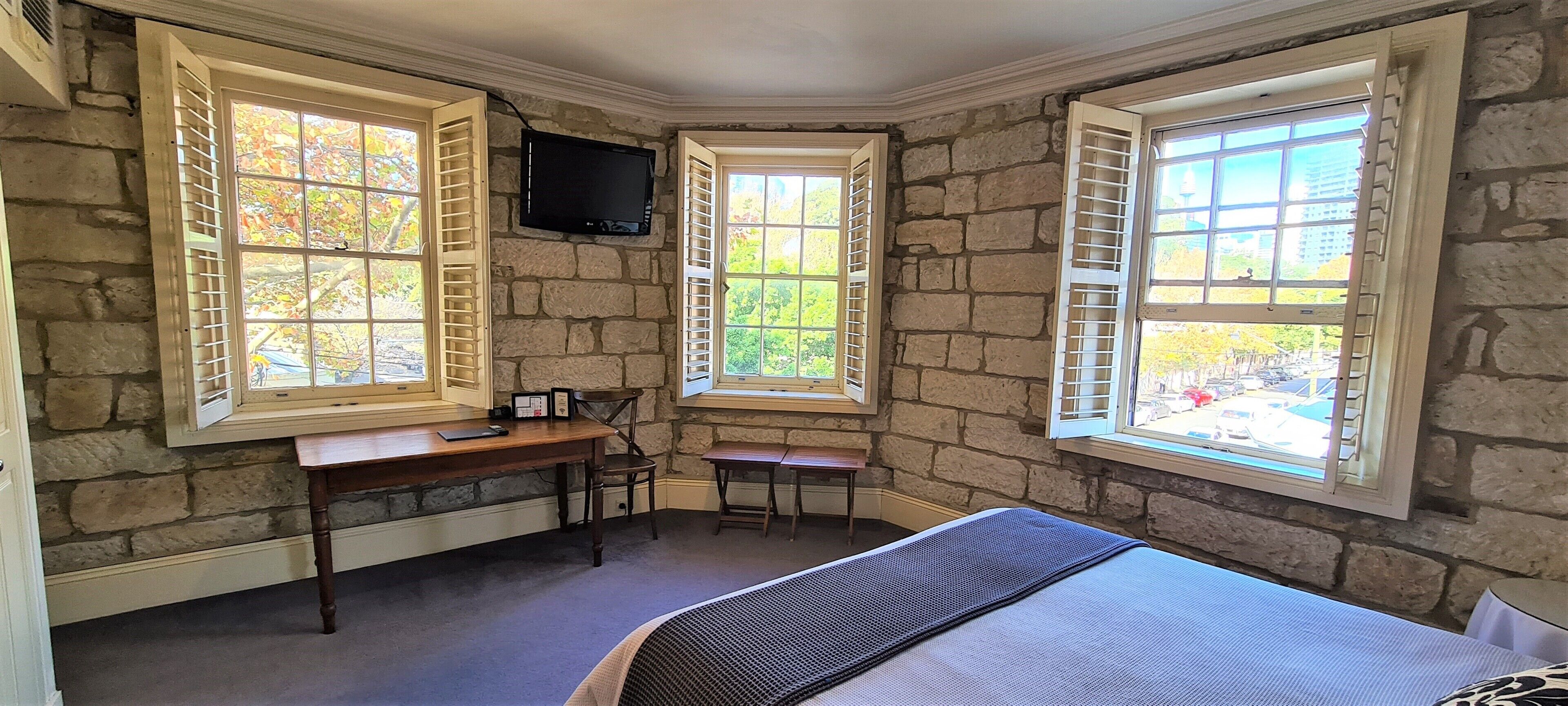 A bedroom with stone walls, a desk, a chair, a bed, and a TV mounted on the wall.