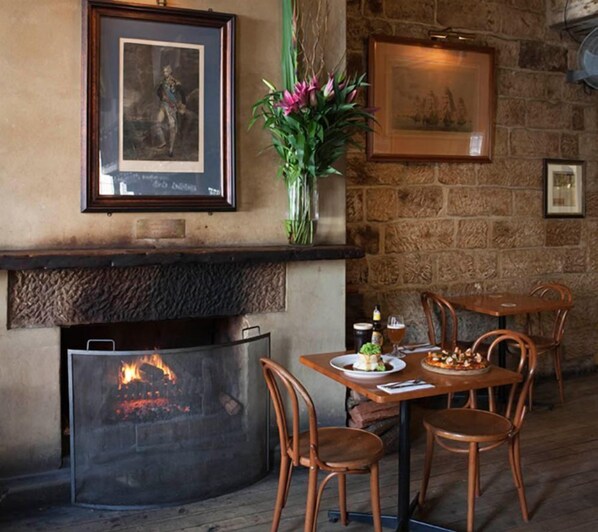 Un rincón comedor acogedor con chimenea, sillas de madera y una mesa dispuesta para dos.