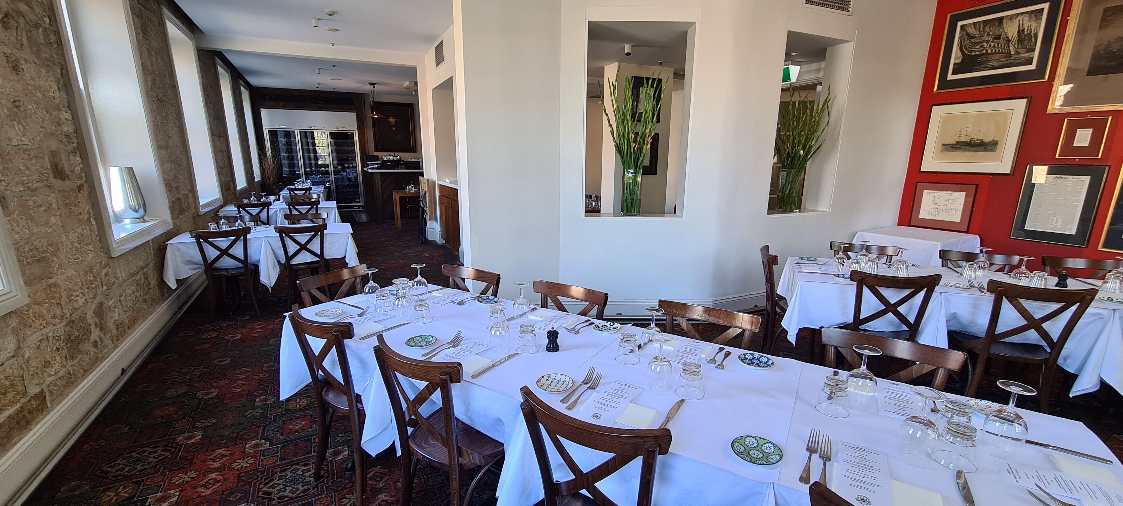 A restaurant with multiple tables set for dining, featuring white tablecloths and wooden chairs.