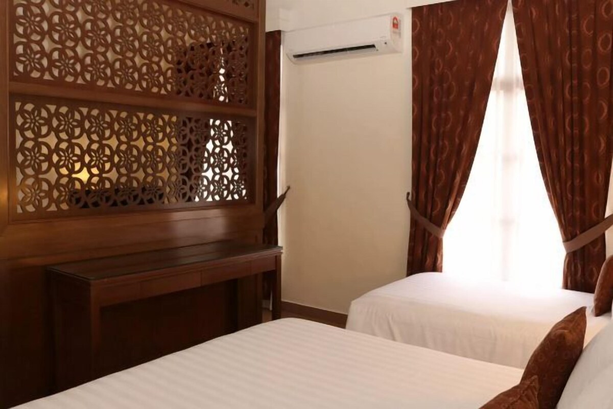 A hotel room with two beds, a wooden partition with intricate cut-out designs, an air conditioning unit, and brown curtains.