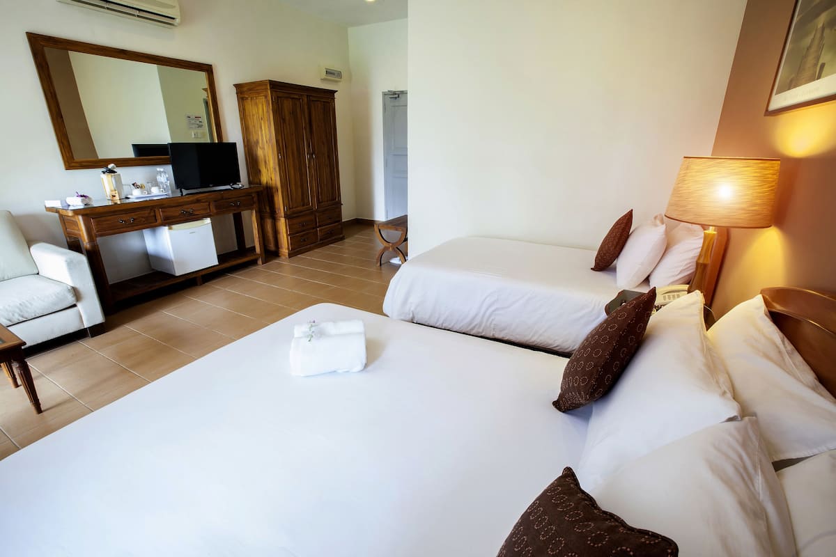 A hotel room with two beds, a desk with a television, a wardrobe, and a bathroom in the background.