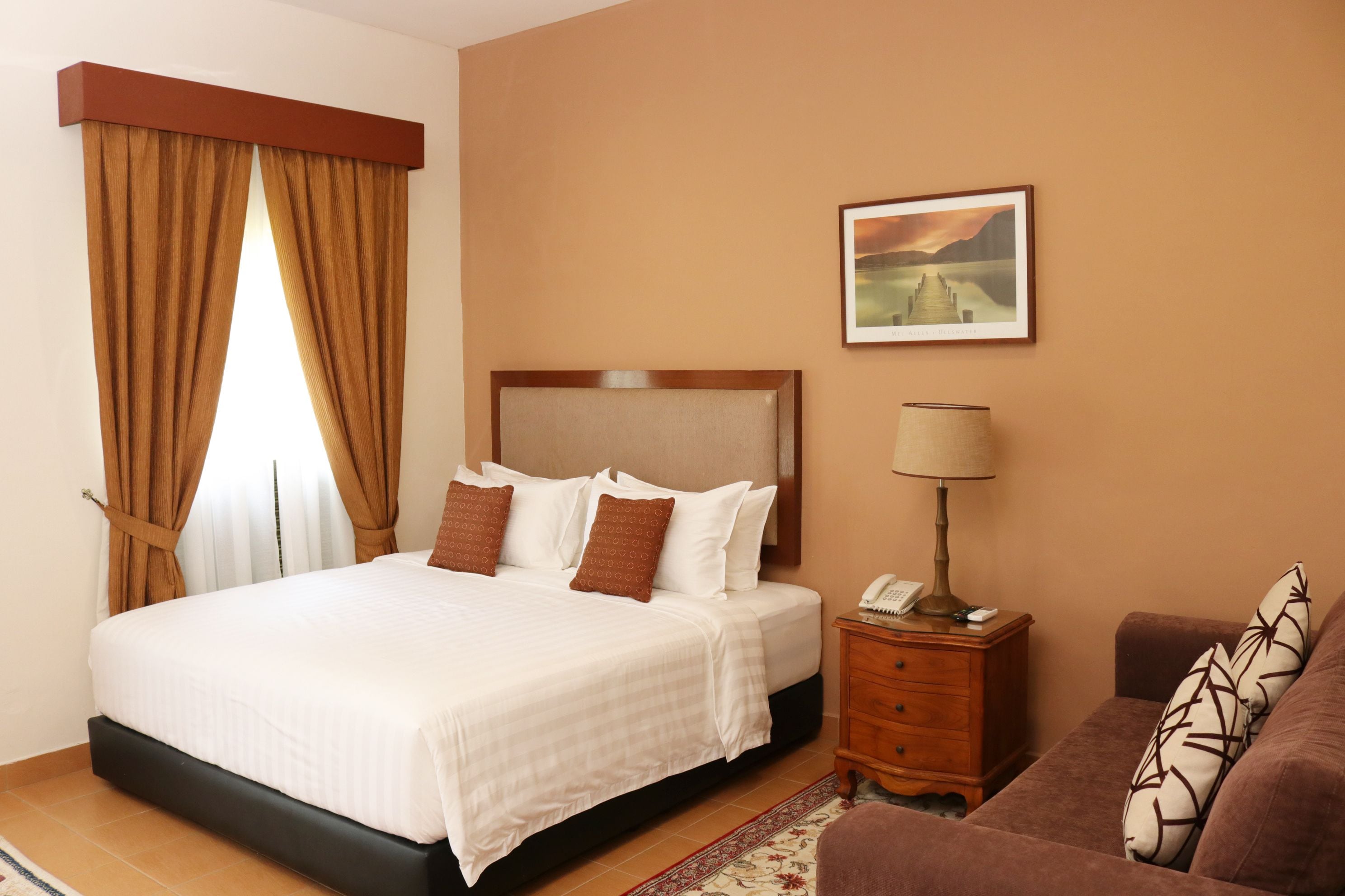 Una camera d'albergo con un letto grande, un comodino con una lampada, un divanetto e un quadro appeso al muro.