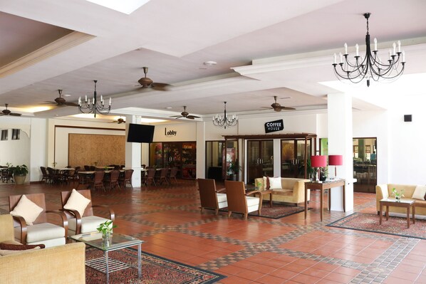 Um hall amplo com uma cafeteria, áreas de estar confortáveis e um lustre moderno.