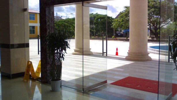 A glass entrance with white columns, a potted plant, and a red mat. - Royal Hotel Luang Namtha ' Huang Ching' (Luang Namtha)