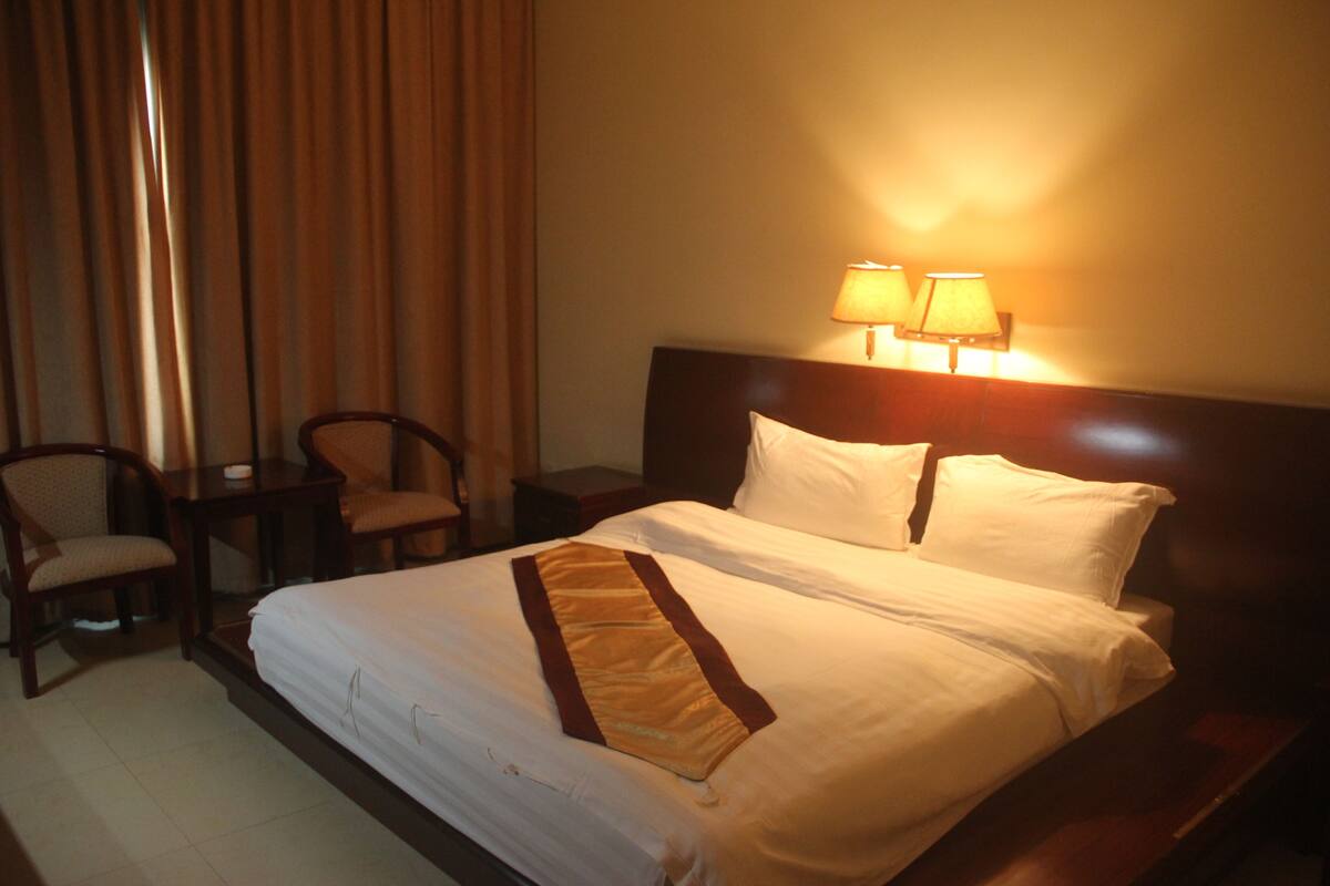 A hotel room with a neatly made bed, two bedside lamps, a chair, and a small table.