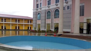 A large outdoor swimming pool surrounded by buildings with yellow and pink facades. - Royal Hotel Luang Namtha ' Huang Ching' (Luang Namtha)