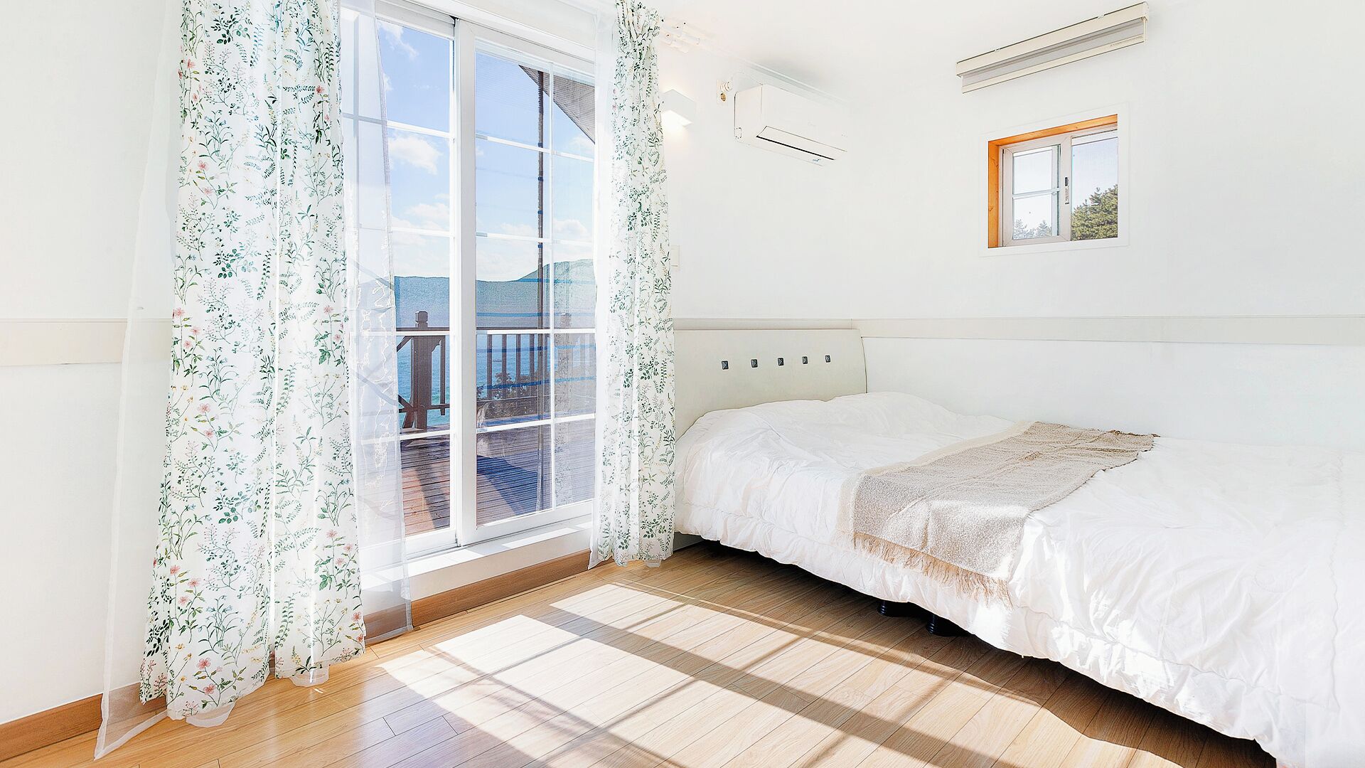 Ein Schlafzimmer mit großem Fenster, einem Bett und einem kleinen Bilderrahmen an der Wand.