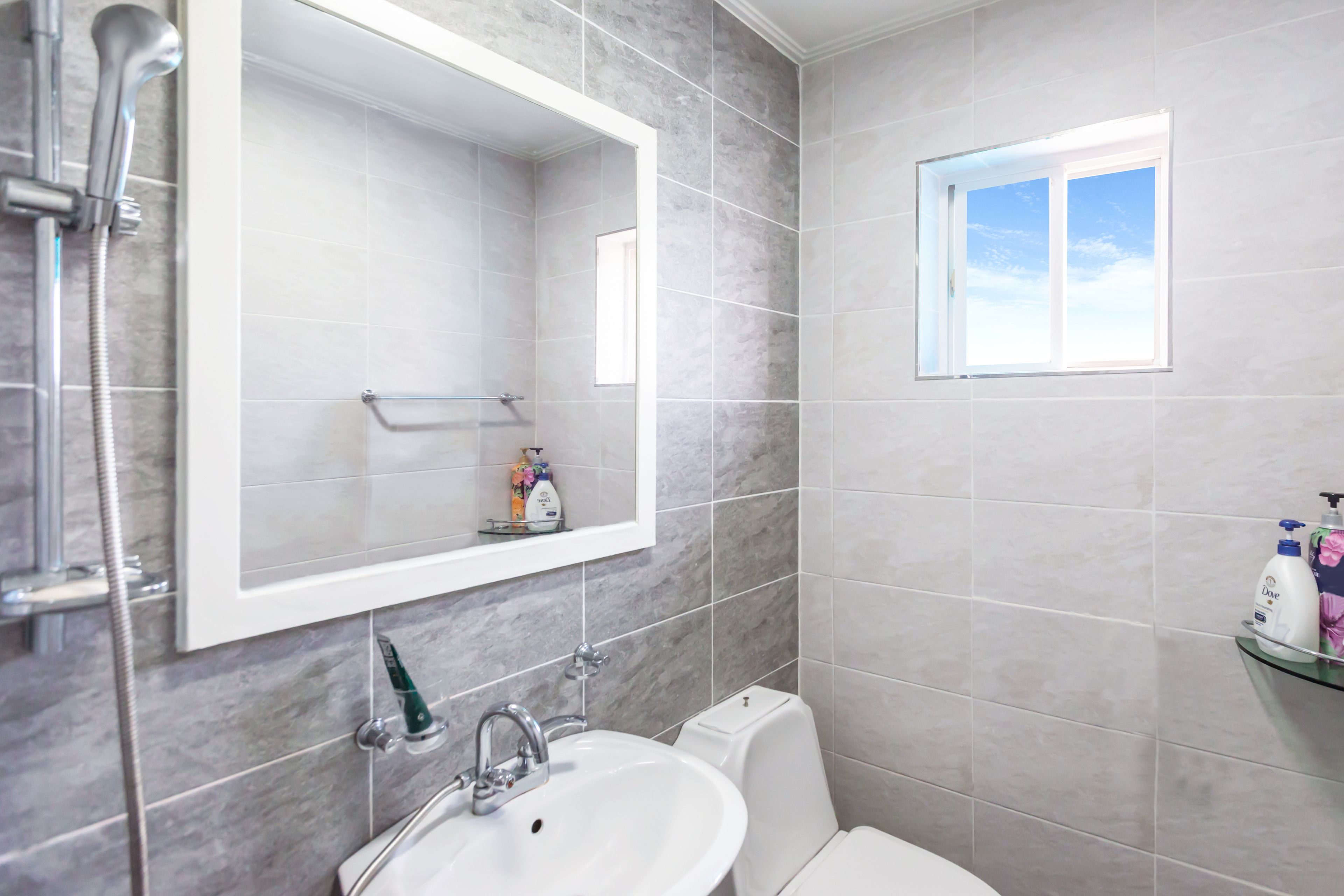 A bathroom with a white sink, a mirror, a shower, and a window.