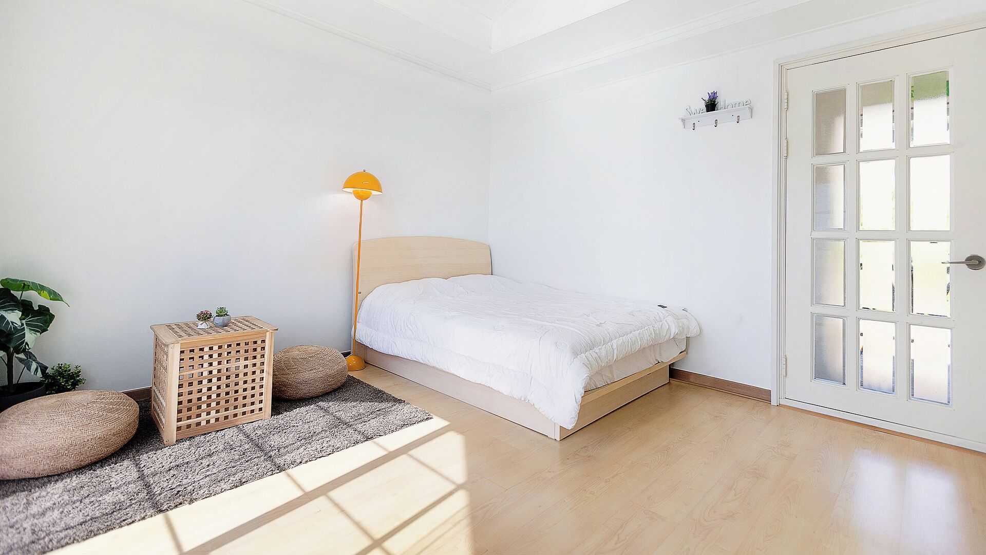 Un dormitorio minimalista con cama, una lámpara de pie y una puerta con paneles de vidrio esmerilado.