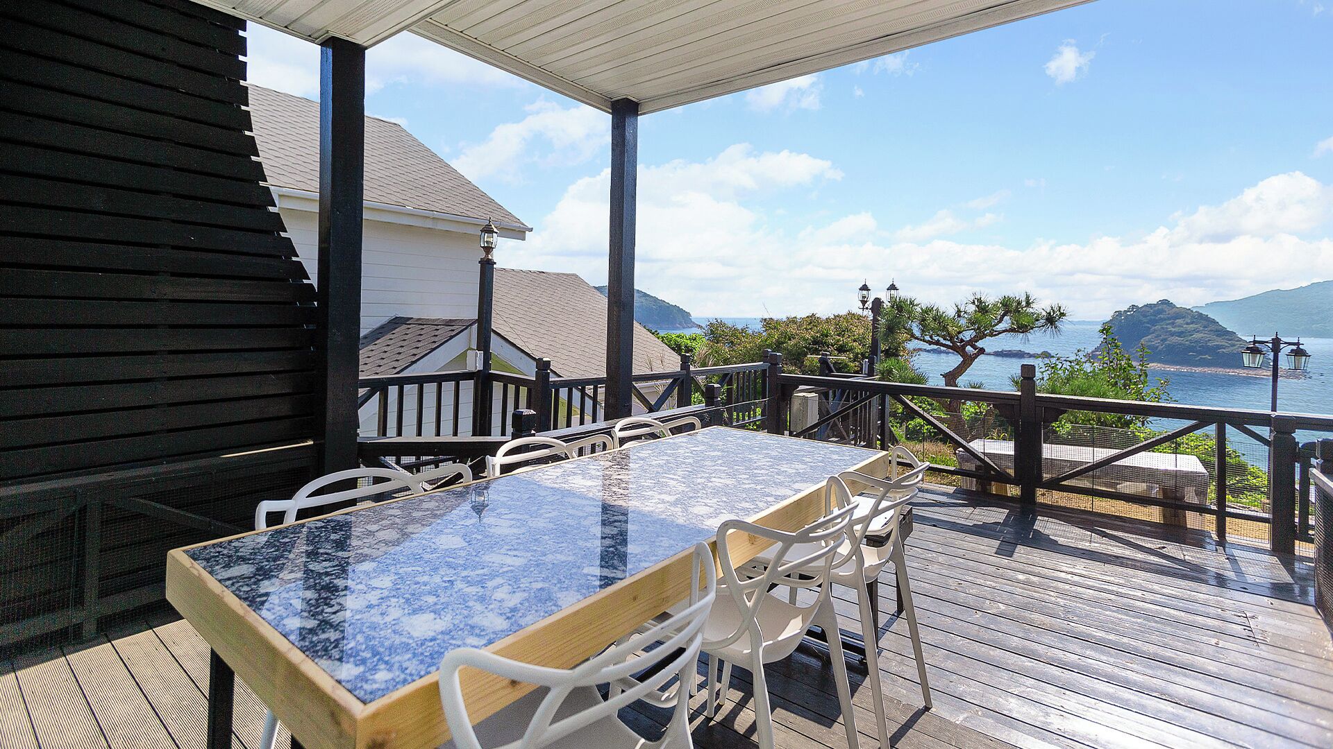 A wooden deck with a table and chairs, overlooking a body of water and hills.
