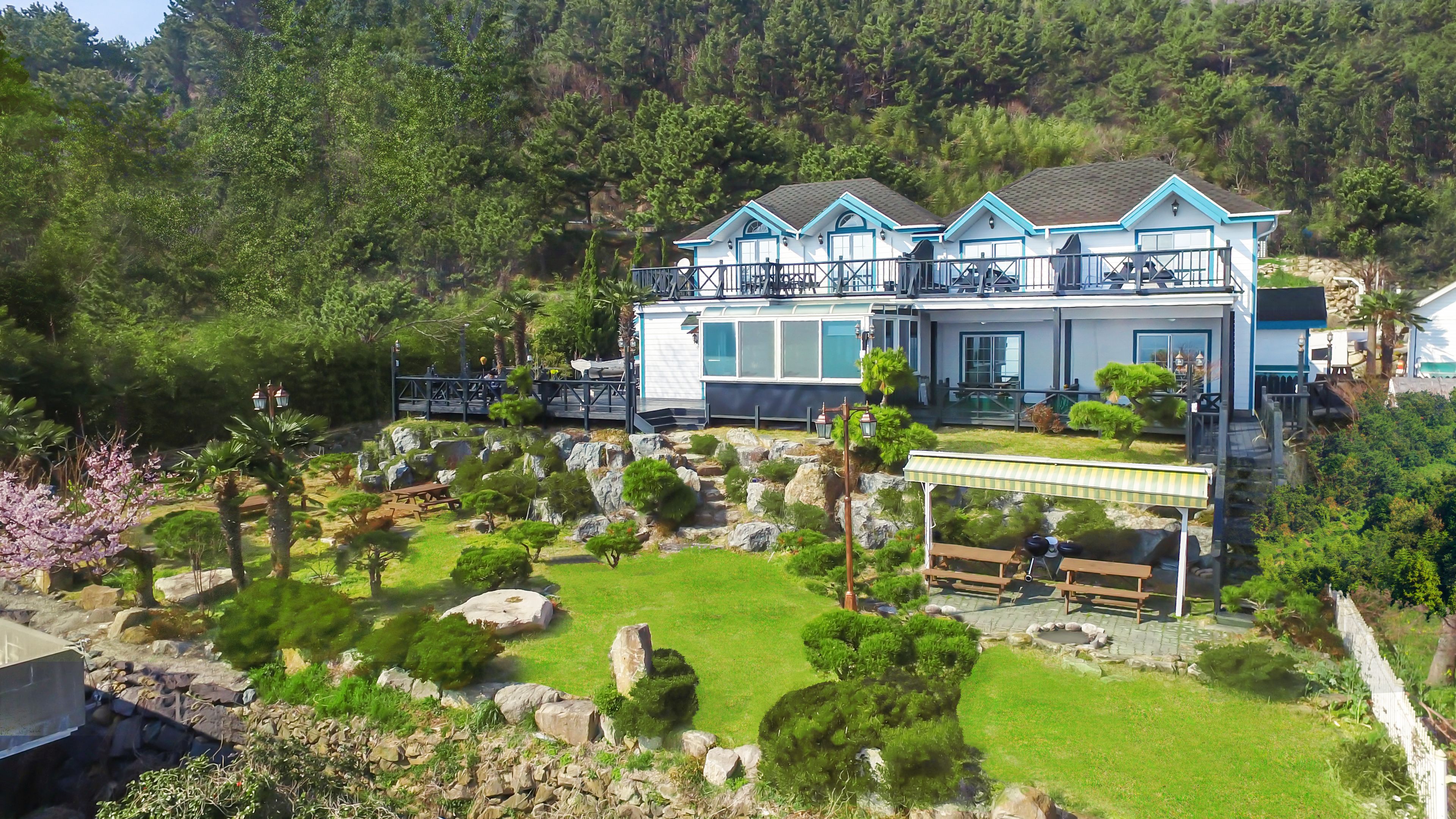 A two-story house with a balcony, surrounded by a well-maintained garden with various plants and a small pond.