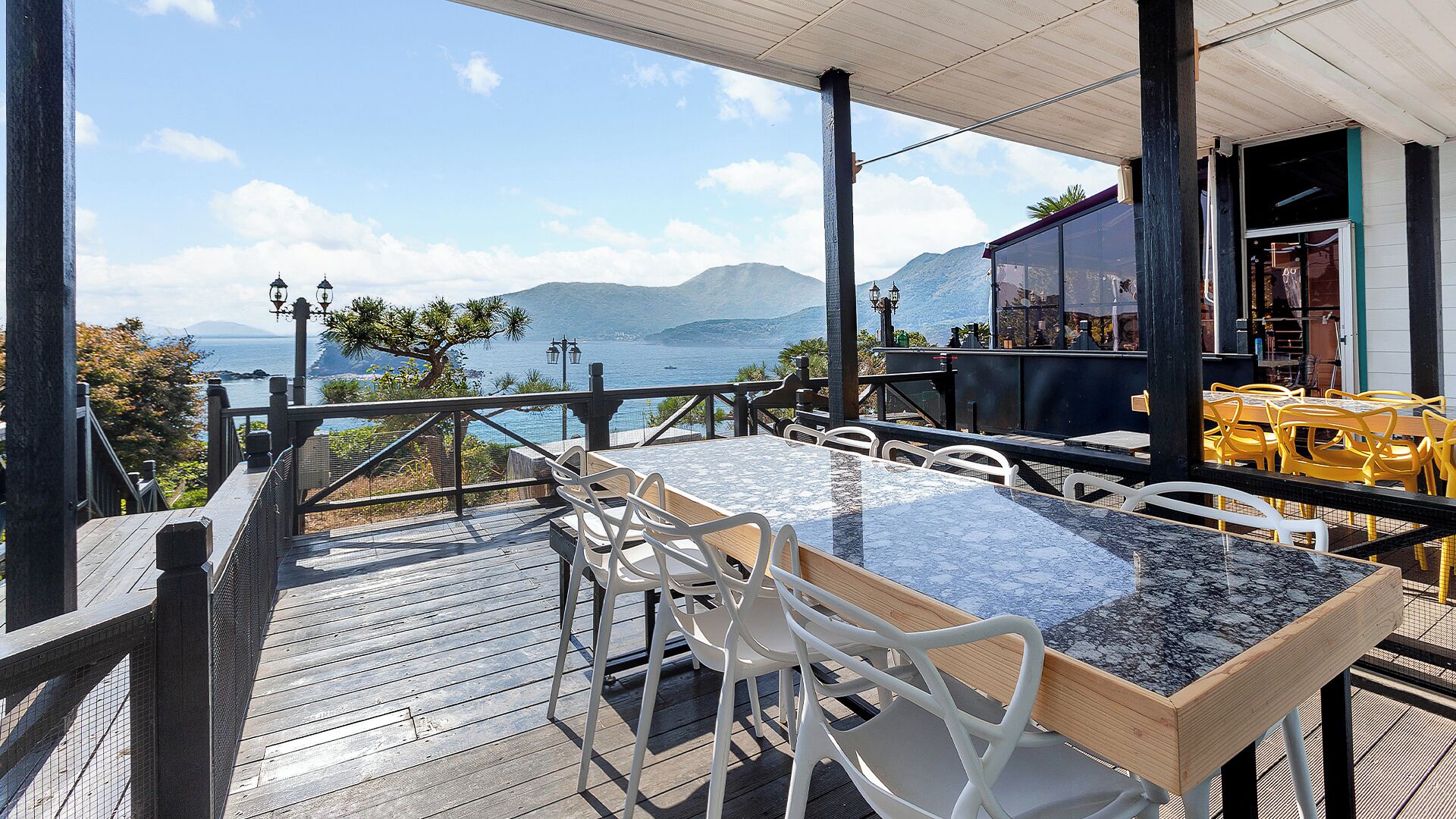 En terrasse med et bord og stole med udsigt over et smukt hav- og bjerglandskab.