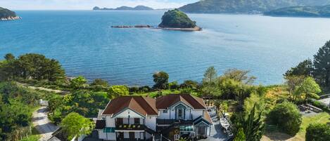 A coastal property with a large house featuring a balcony and a small boat docked outside.