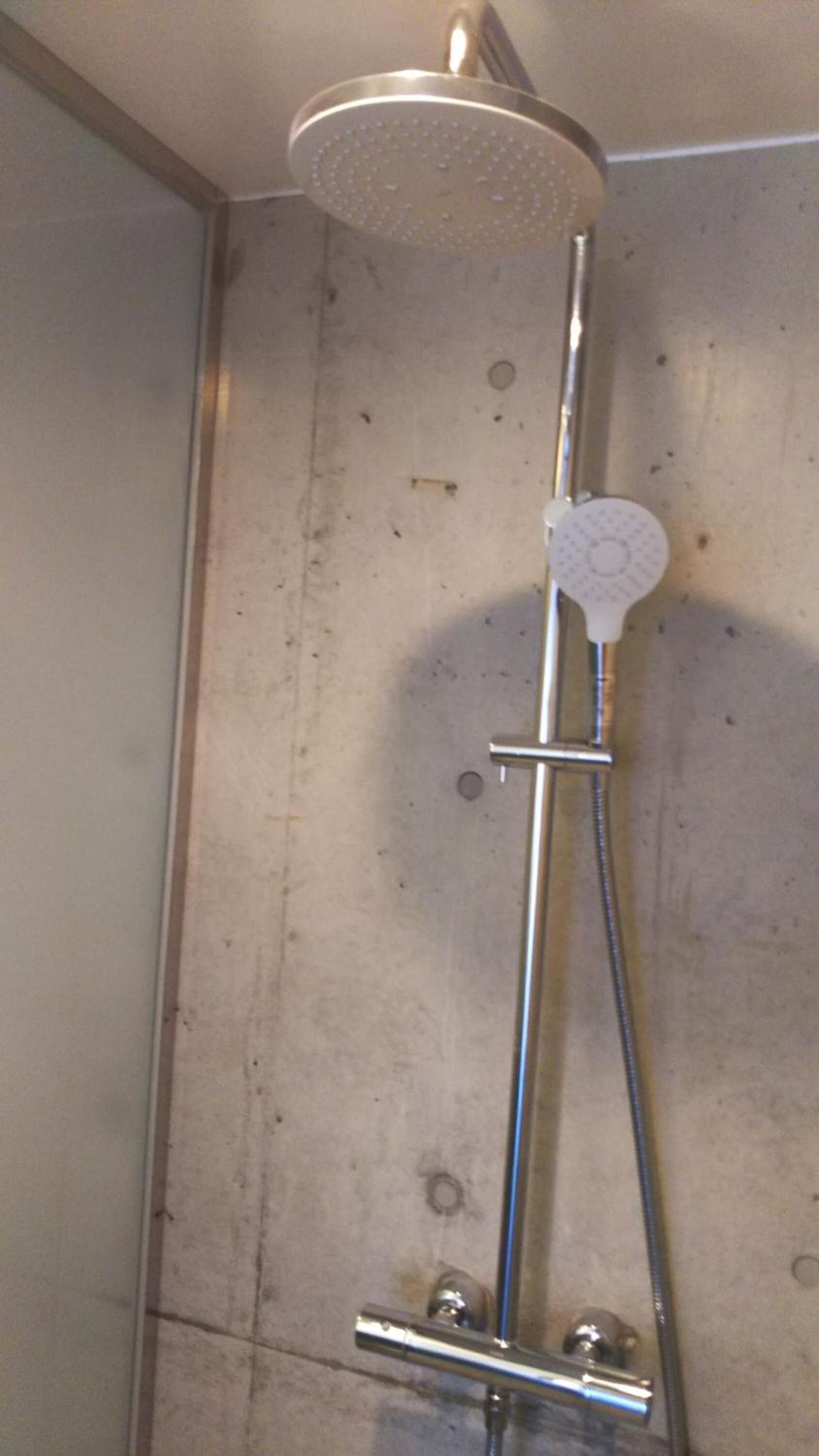 A shower with a handheld head, a vertical bar, and a wall-mounted control.