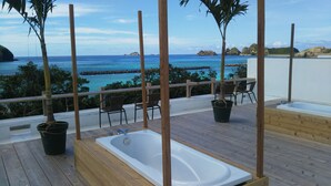 A wooden deck with a bathtub, chairs, and potted plants overlooking a beach and ocean. - Blue Suites Hanamuro on the beach (Zamami)