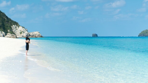A beach with clear turquoise water and a person standing on the shore. - Blue Suites Hanamuro on the beach (Zamami)
