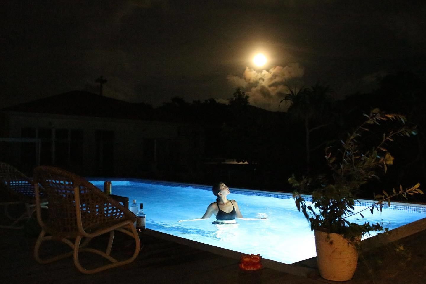 Una persona en una piscina de noche, con una luna llena en el cielo.