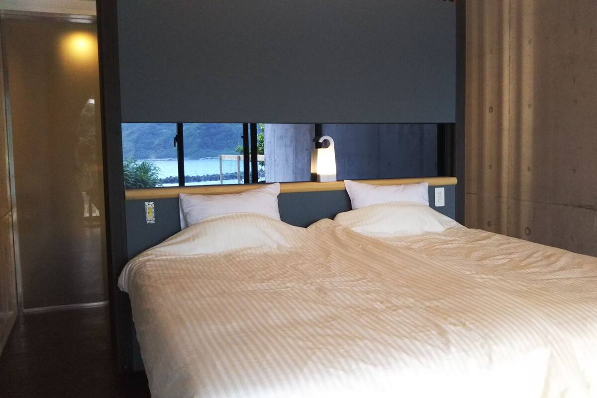 Ett hotellrum med en säng, utsikt över havet och ett fönster med gardiner.