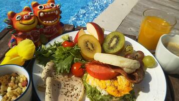 A meal with fruits, vegetables, and a drink by a poolside.
