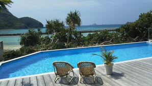 A swimming pool with two wicker chairs and a potted plant on a wooden deck, overlooking a tropical beach and clear blue sea. - Blue Suites Hanamuro on the beach (Zamami)