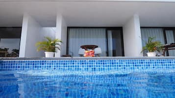 Una piscina con borde de azulejos, dos macetas, una silla y una mesa con lámpara.