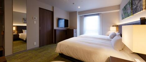 A hotel room with a large bed, a flat-screen TV, a desk with a lamp, and a window with curtains.