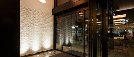 A modern hotel lobby with patterned walls, a carpeted floor, and glass doors leading to the reception area.
