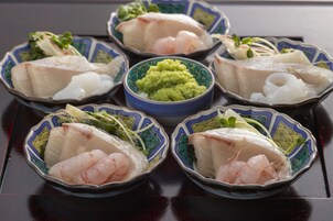 Una mesa con seis cazos de sashimi, cada uno con diferentes tipos de pescado y guarniciones, y un cazo central de salsa verde.