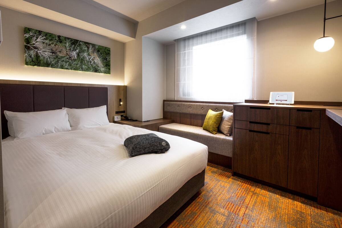 A hotel room with a large bed, a seating area with cushions, a desk with a computer, and a window with curtains.