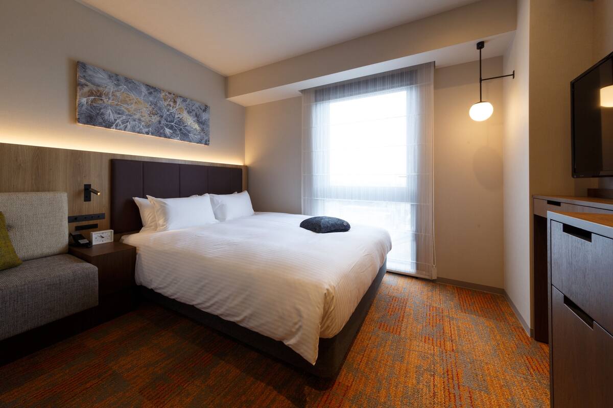 A hotel room with a large bed, a small sofa, a desk, and a window with curtains.