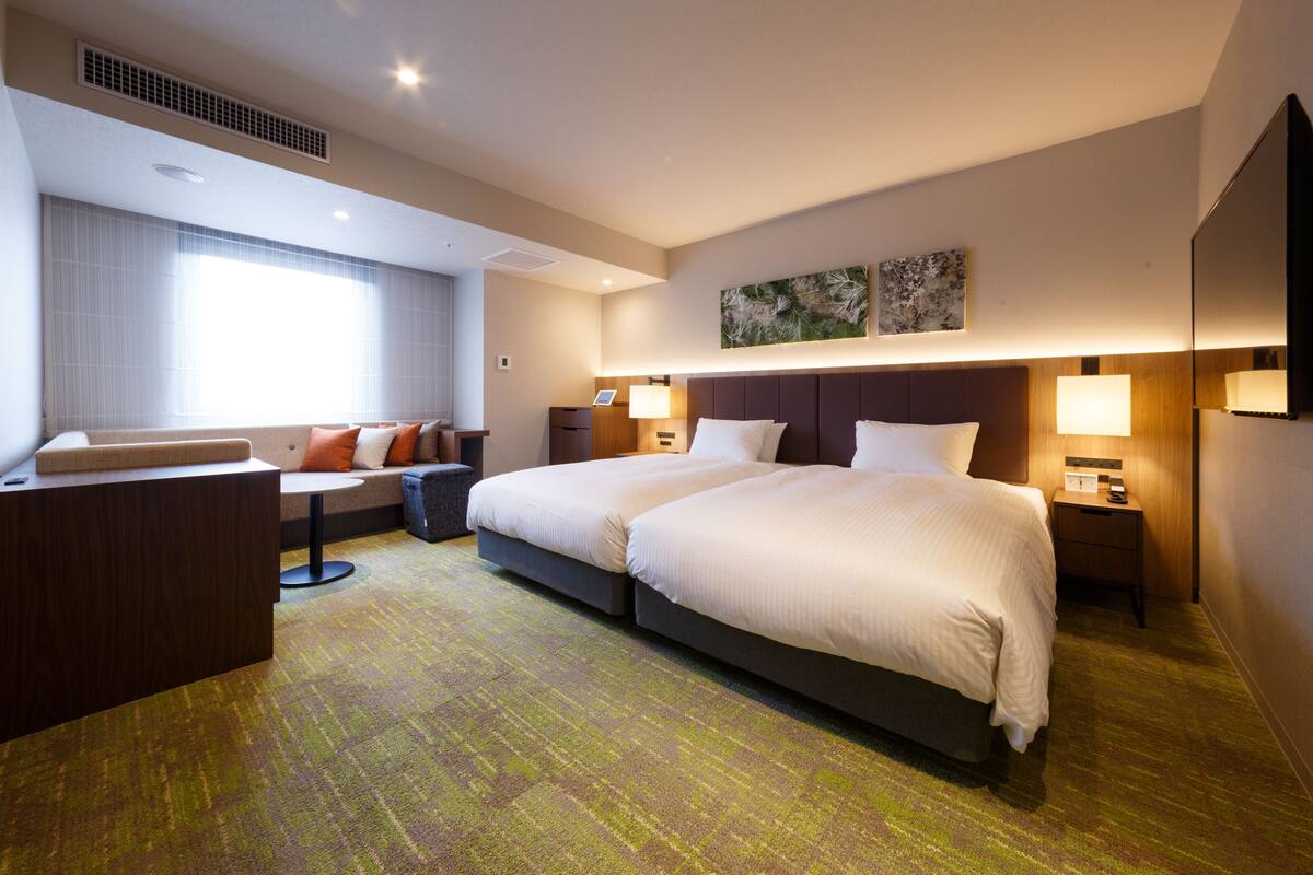 A hotel room with a large bed, a sofa, a desk, and a window with curtains.
