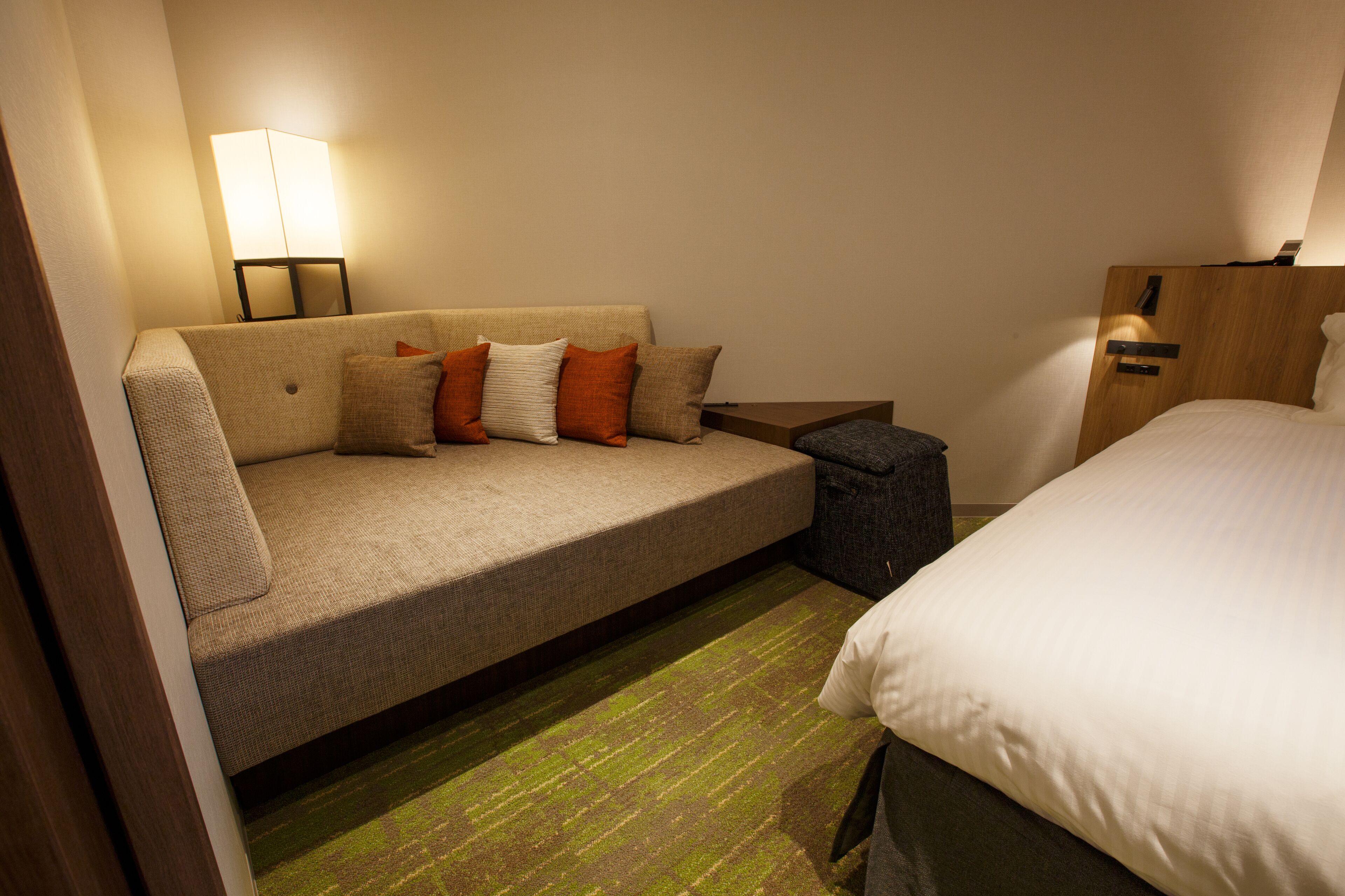 A hotel room with a sofa, a bed, a nightstand, and a lamp.